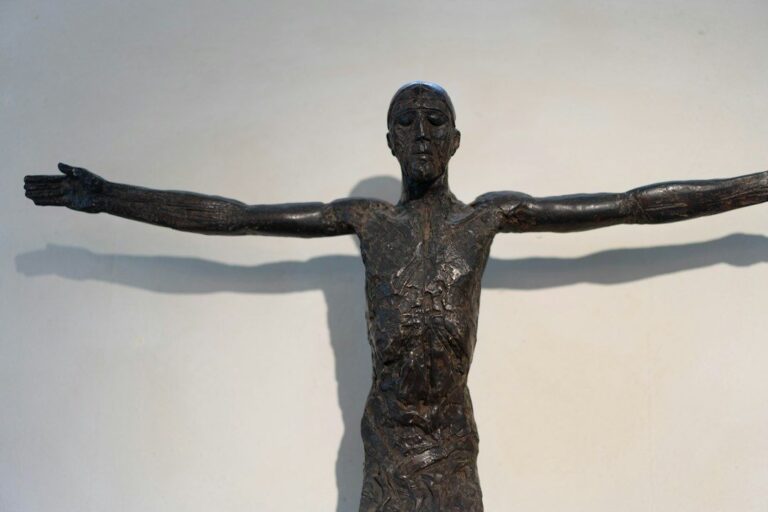 Dunkle Bronzeskulptur eines Menschen mit weit ausgebreiteten Armen im Museum